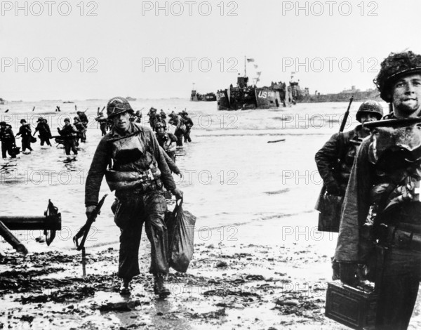 American assault troops, carrying full equipment, moving onto beachhead, landing craft jam harbor in background, Omaha Beach, Normandy, France, U.S. Army Signal Corps, June 6, 1944