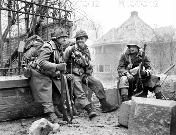 American Infantrymen pause to rest en route to front lines, Left to right, Sgt. Lyle Greene, Rochester Minnesota, S/Sgt. Joseph DeMott, Greenwood, Ind., and Pfc. Fred Mozzoni, Chicago, Illinois, near Malmedy, Belgium, U.S. Army Signal Corps, December 29, 1944