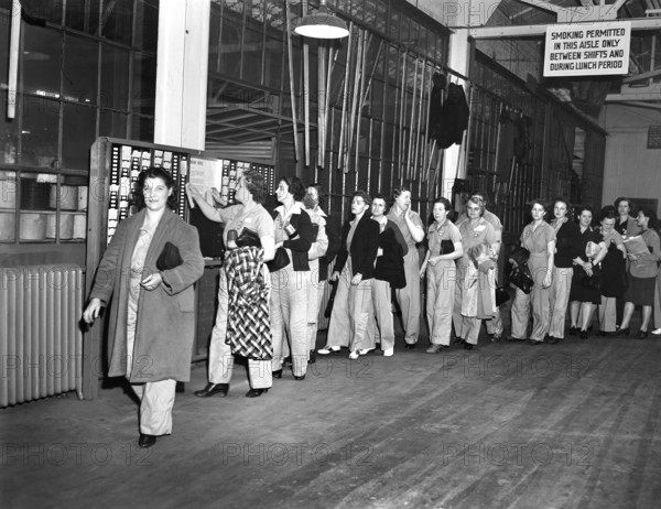 Women war workers wearing slacks punching time cards at end of shift, De Soto bomber plant, Detroit, Michigan, USA, Arthur S. Siegel, U.S. Office of War Information, October 1942
