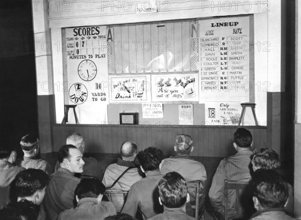 Officers and enlisted men of 2nd Infantry Division, 1st U.S. Army watching board giving them play-by-play description of Army-Navy football game at their Headquarters, Vith, Belgium, U.S. Army Signal Corps, December 2, 1944