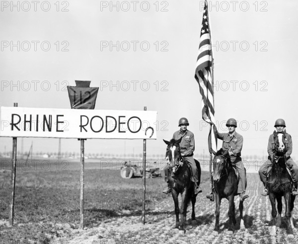 Infantrymen of the 28th Division, U.S. First Army, stage a rodeo on bank of Rhine River while shells are bursting a few miles away on opposite side of river, Karlick, Germany, U.S. Army Signal Corps, March 25, 1945