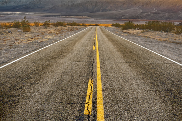Two-lane asphalt road with mountains in background, diminishing perspective, Death Valley National Park, California, USA