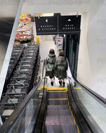 Rear view of two women descending escalator at supermarket, Brooklyn, New York, USA