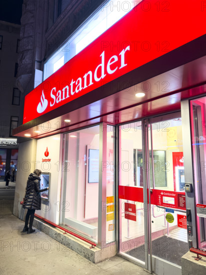 Santander retail bank office, woman using outdoor ATM machine at night, New York City, New York, USA