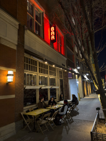 Group of people sitting at sidewalk bar at night, New York City, New York, USA