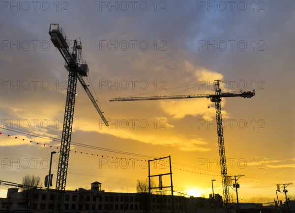 Two silhouetted construction cranes at sunset