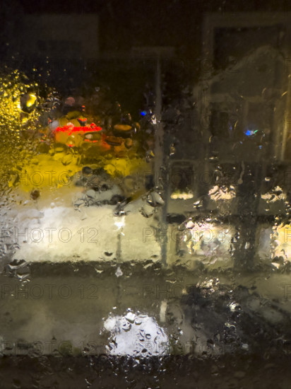 Blurred street scene viewed through window with dripping raindrops at night