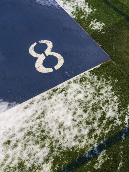 High angle view of number 8 on blue background surrounded by green synthetic grass dusted with snow