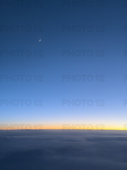 Crescent moon in deep blue sky at sunset viewed through airplane window
