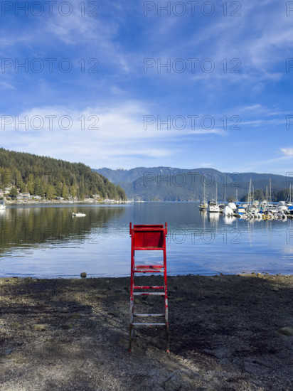 Red lifeguard chair on beach with houses on left and sailboats on right, Port Moody, North Vancouver, British Columbia, Canada