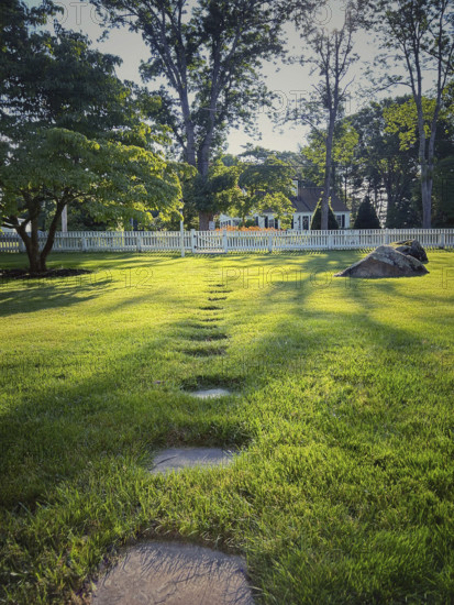 Residential front yard with stone pathway through green lawn to picket fence