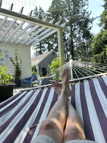 View of mid-adult man's bare legs and feet while relaxing in hammock on summer day
