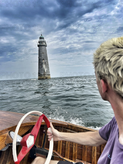 Young adult man driving vintage motor boat near lighthouse