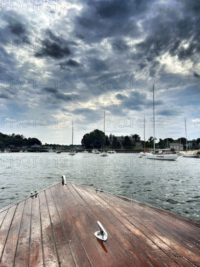 Bow of vintage wood boat with moored harbor sailboats in background