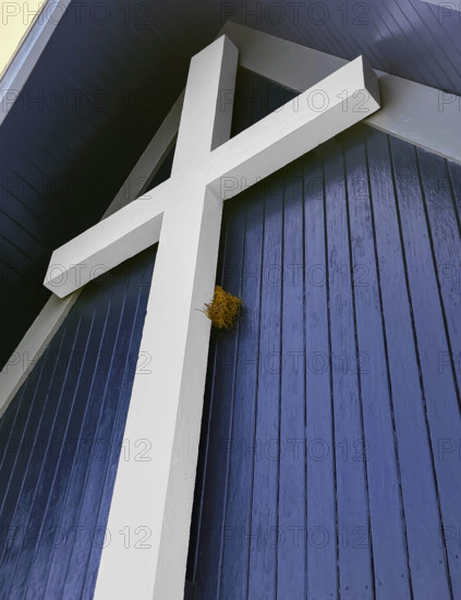 Bird nest tucked behind large white religious cross on building exterior, low angle view