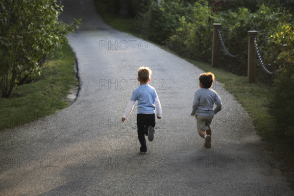 Rear view of two young boys running down paved driveway