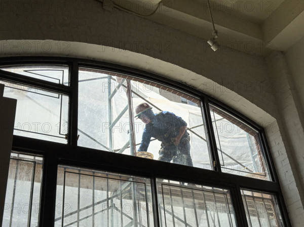 Construction worker repairing building façade, viewed through residential apartment window, Manhattan, New York City, New York, USA