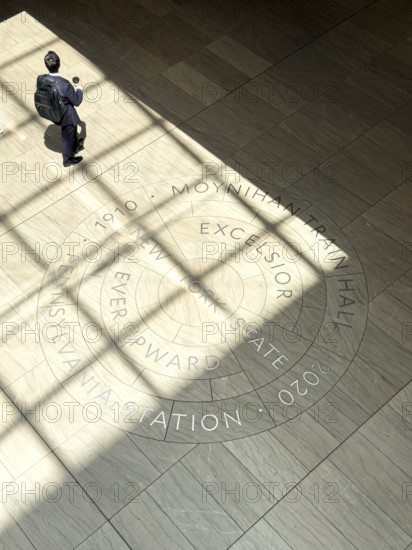 High angle view of commuter walking across New York State motto engraved on floor of Moynihan Train Hall, Pennsylvania Station, Manhattan, New York City, New York, USA