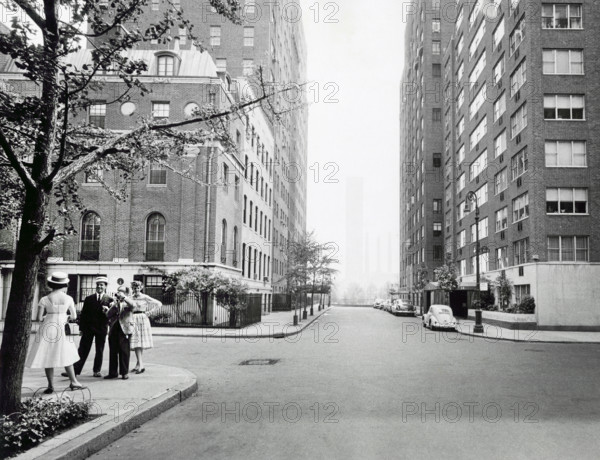 Small group of people standing left with photographer taking photograph of one woman in a hat and dress, south view of Beekman Place at  corner of East 50th Street, Turtle Bay neighborhood, Manhattan, New York City, New York, USA, Angelo Rizzuto, Anthony Angel Collection, June 1958
