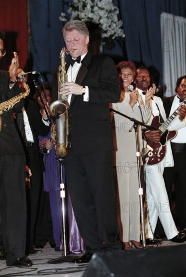 U.S. President Bill Clinton playing saxophone, as singer Dionne Warwick and others look on, at one of his inauguration balls, Arkansas Inaugural Ball, Washington Convention Center, Washington, D.C., USA, Bob McNeely, White House Photographer, January 20, 1993