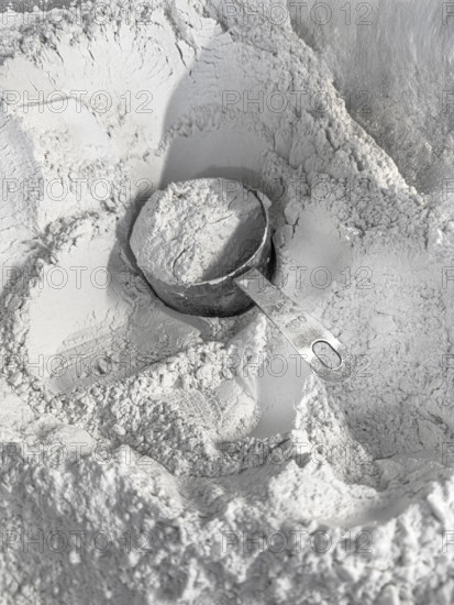 Full measuring cup of flour sitting in a mound of flour