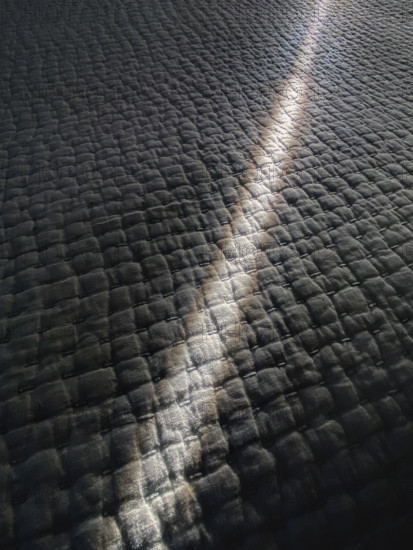 Stream of sunlight shining through gap in curtains onto bedspread