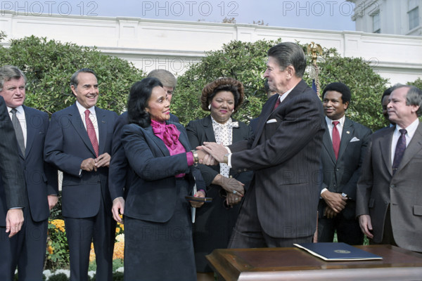 U.S. President Ronald Reagan shaking hands with Coretta Scott King at signing ceremony for HR 3706 making birthday of Martin Luther King Jr a national Holiday, with Howard Baker, Bob Dole, Katie Hall and Edward Kennedy looking on, White House Rose Garden, Washington, D.C., USA, President Ronald Reagan White House Photographic Office, November 2, 1983