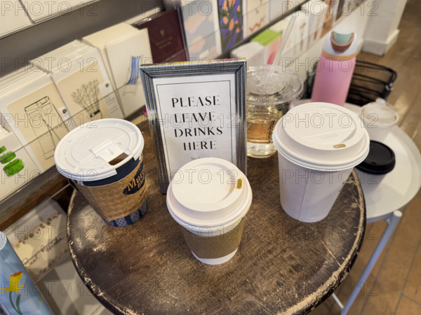 "Please leave drinks here" framed sign on round wood table with paper and plastic cups in retail store