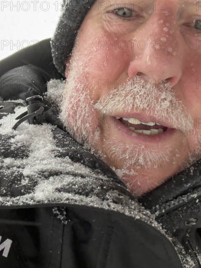 Head and shoulders portrait of mature adult man with face covered in snow and ice