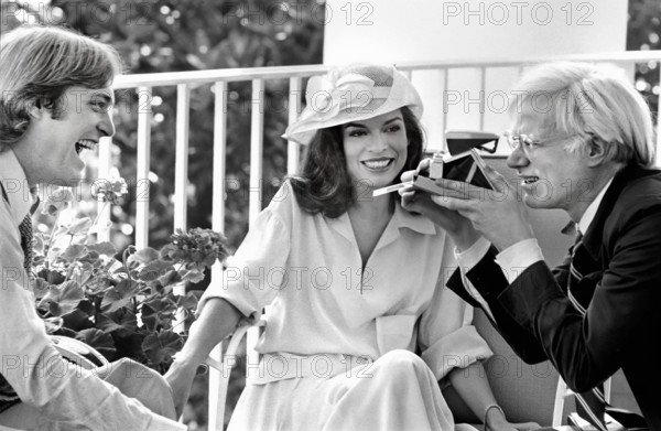 American artist Andy Warhol taking Polaroid picture while sitting with Jack Ford and Bianca Jagger on White House Truman Balcony, Washington, D.C., USA, Gerald R. Ford White House Photographs, July 2, 1975