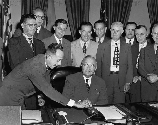 U.S. President Harry S. Truman seated at his desk preparing to push button activating a new generator at Grand Coulee Dam, as unidentified members of Congress from a number of Western states look on, White House Oval Office, Washington, D.C., USA, Abbie Rowe, National Parks Service, Harry S. Truman Library, May 20, 1949