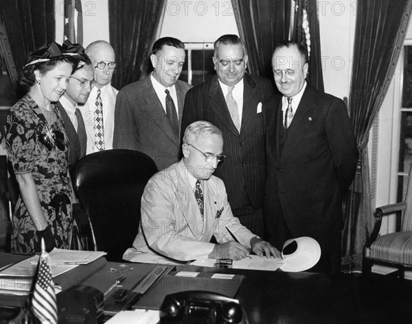 U.S. President Harry S. Truman (seated) in the White House Oval Office signing bill to make governorship of Puerto Rico an elected office as Governor of Puerto Rico Jesus T. Pinero (standing, 2nd right), and Puerto Rico Resident Commissioner Antonio Fernos Isern (standing right) look on, Washington, D.C., USA, Abbie Rowe, National Parks Service, Harry S. Truman Library, August 5, 1947