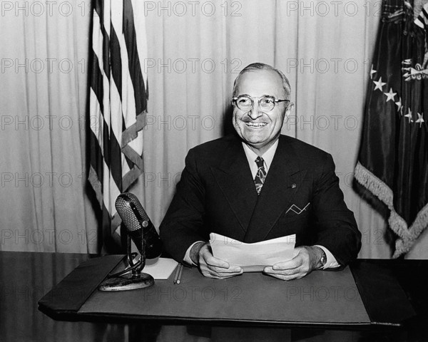 U.S. President Harry S. Truman smiling for photographers while delivering radio speech to the nation concerning the reconversion program for a peacetime economy, White House Oval Office, Washington, D.C., USA, Abbie Rowe, National Parks Service, Harry S. Truman Library, January 3, 1946