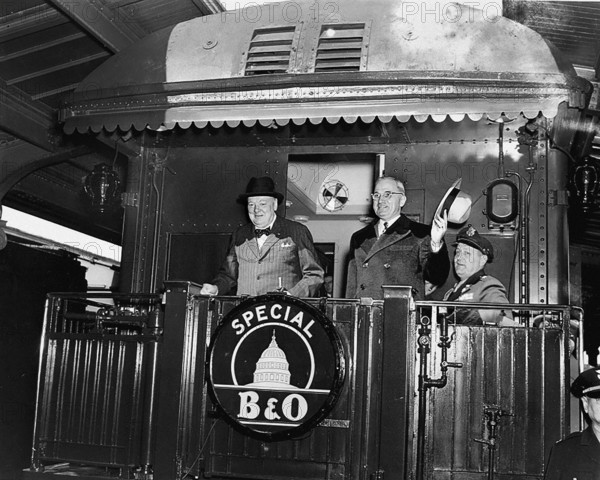 U.S. President Harry S. Truman (right) waving his hat standing to right of former British Prime Minister Winston Churchill on rear platform of special Baltimore & Ohio train, en route to Fulton, Missouri for Churchill's "Iron Curtain" speech, as President's Military Aide, General Harry Vaughan, looks on, Washington, D.C., USA, Abbie Rowe, National Parks Service, Harry S. Truman Library, March 4, 1946