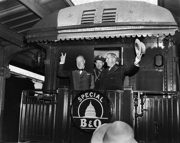 U.S. President Harry S. Truman (right) waving his hat standing to right of former British Prime Minister Winston Churchill flashing his famous "V for Victory" sign from rear platform of special Baltimore & Ohio train, en route to Fulton, Missouri for Churchill's "Iron Curtain" speech, as President's Military Aide, General Harry Vaughan, looks on, Washington, D.C., USA, Abbie Rowe, National Parks Service, Harry S. Truman Library, March 4, 1946