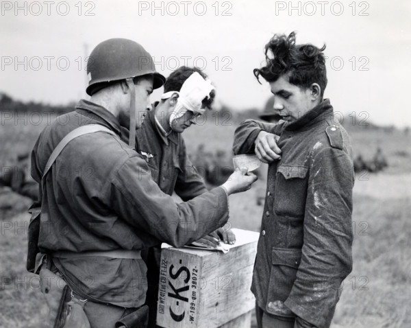 American soldier making out identity tag for young German prisoner of war as another wounded Nazi supplies necessary information, Normandy, France, U.S. Army Signal Corps, June 9, 1944
