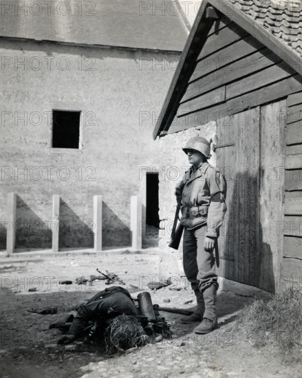 U.S. military police standing guard in barnyard near body of dead German sniper, Normandy, France, Bowen, U.S. Army Signal Corps, June 15, 1944
