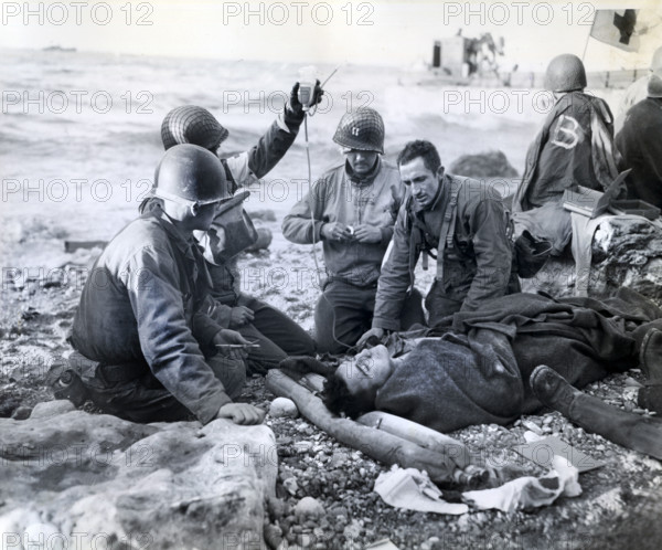U.S. Army medical soldiers, just a few feet from the surf, administering plasma transfusion to survivor of sunk landing craft, Normandy, France, U.S. Army Signal Corps, June 1944