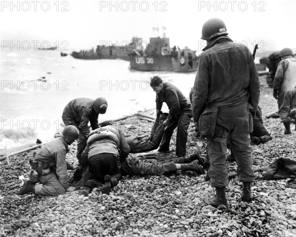 American soldiers applying artificial respiration on two other soldiers who reached the north coast of France in rubber life raft after their landing craft was sunk by enemy action while several hundred yards from shore, near Cherbourg, Normandy, France, Weintraub, U.S. Army Signal Corps, June 6, 1944