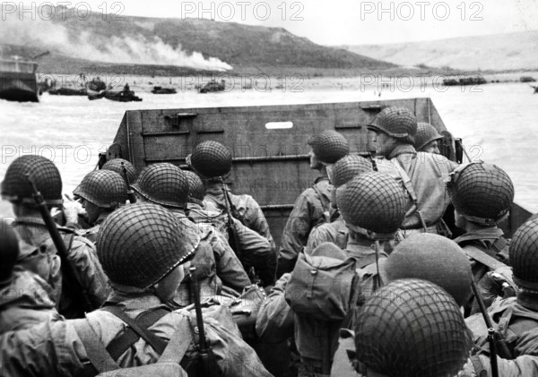 American assault troops in landing craft huddling behind protective front of craft as it nears beachhead, as smoke from naval gunfire supports the landing in background, Northern Coast of France, U.S. Army Signal Corps, June 6, 1944