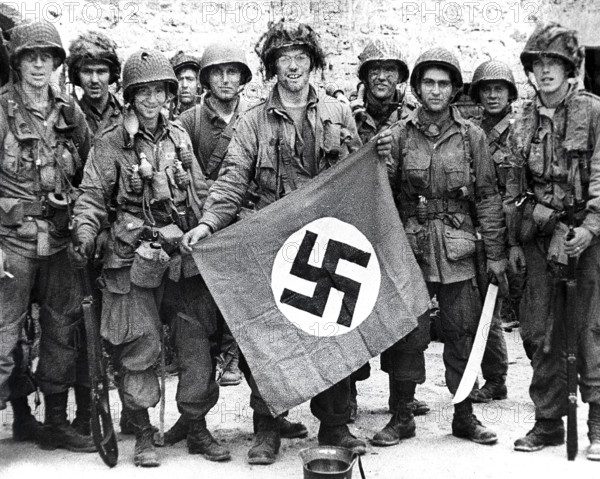 American paratroopers, among the first to make successful landings on European continent, holding Nazi flag captured in village assault, Utah Beach, Saint-Marcouf, Normandy, France, Werner, U.S. Army Signal Corps, June 8, 1944