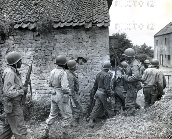 Platoon of Negro troops surrounding farmhouse as they prepare to eliminate a German sniper holding up an advance, Omaha beachhead, near Vierville-sur-Mer, Normandy, France, Todd, U.S. Army Signal Corps, June 10, 1944