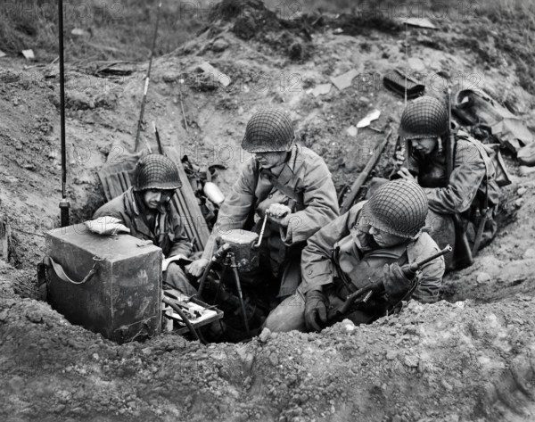 Members of shore fire control party set up "shop" in old shell hole and immediately proceed to direct fire of Naval guns against targets on beach, Normandy, France, U.S. Army Signal Corps, June 10, 1944