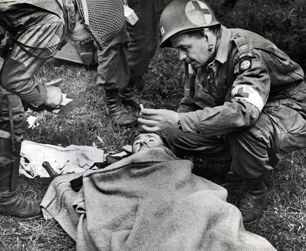 American medical officer, who landed with 82nd Airborne Division, handing lit cigarette to injured solider, Utah Beach, Sainte-Mere-Eglise, Normandy, France, Witscher, U.S. Army Signal Corps, June 7, 1944