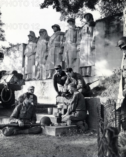Group of American soldiers cooking dinner on GI stove under World War I memorial, near Verdun, France, U.S. Army Signal Corps, September 1, 1944