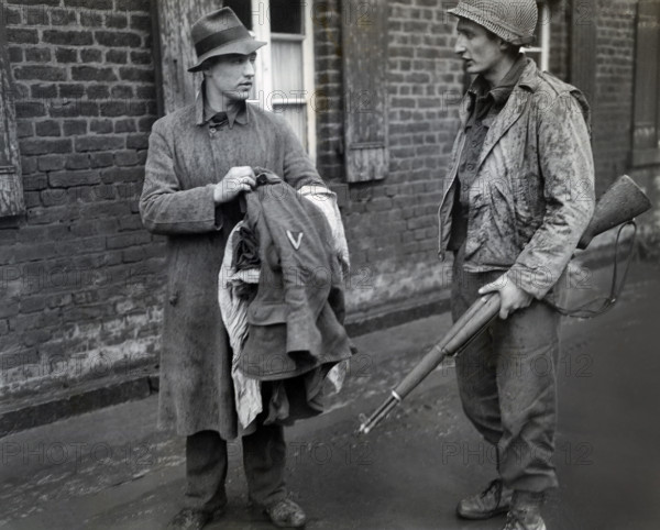 U.S. Staff Sargeant Martin M. Gruenspecht of New York City, New York, member of the 1st Infantry Division, U.S. First Army, being informed by German prisoner that he took off his uniform because he was afraid of being shot by American forces, Bliesheim, North Rhine-Westphalia, Germany, U.S. Army Signal Corps, March 4, 1945