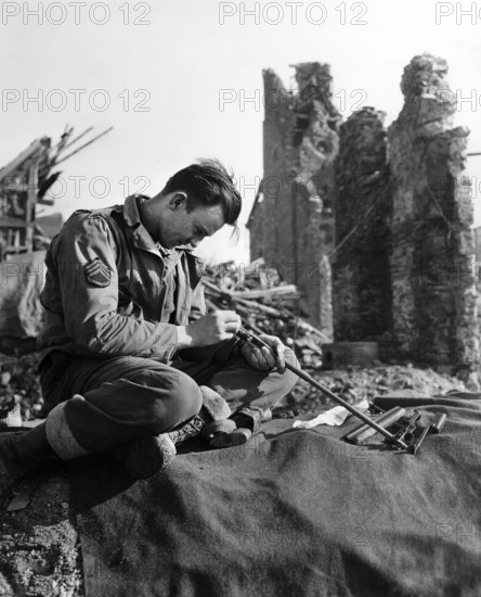 U.S. Staff Sargeant John S. Merger of Cullman, Alabama, 1st Infantry Division, U.S. First Army, taking time to clean his carbine in ruins of town on outskirts of Hurtgen Forest, North Rhine-Westphalia, Germany, U.S. Army Signal Corps, February 15, 1945