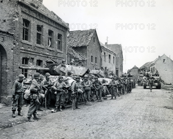 Infantrymen of 1st Division, U.S. First Army, resting beside military tanks, Monchengladbach, North Rhine-Westphalia, Germany, U.S. Army Signal Corps, March 1, 1945