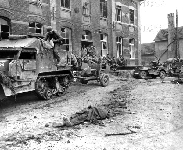 Members of Company G, 2nd Battalion, 16th regiment, 1st Division, U.S. First Army with military half-track hybrid vehicle waiting for orders to move on, as dead German soldier lays on ground in foreground, Vetteweiss, Germany, U.S, Army Signal Corps, February 28, 1945