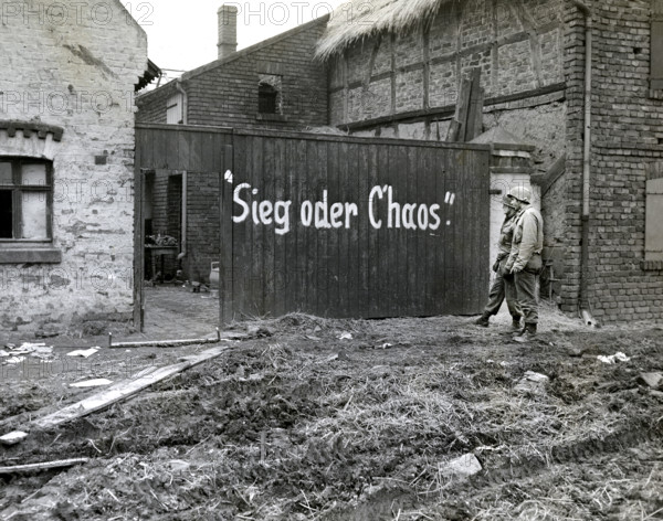 Two members of 1st Engineer Battalion, 16th regiment, 1st Division, U.S. First Army, reading sign written by German troops when they pulled out "Sieg oder Chaos", English translation, "Victory or Chaos", Vetteweiss, Germany, U.S, Army Signal Corps, February 28, 1945